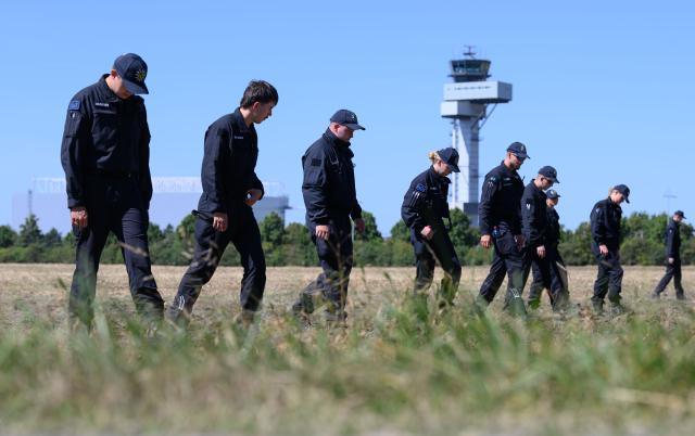 12 August 2026, Saxony, Schkeuditz: Police officers search a field at Leipzig/Halle Airport for evidence. An investigation is underway following the drone incident that occurred on August 5th, 2026. According to security sources, the drone-which was equipped for an attack-was seized near a Ukrainian transport aircraft. Photo: Hendrik Schmidt/dpa