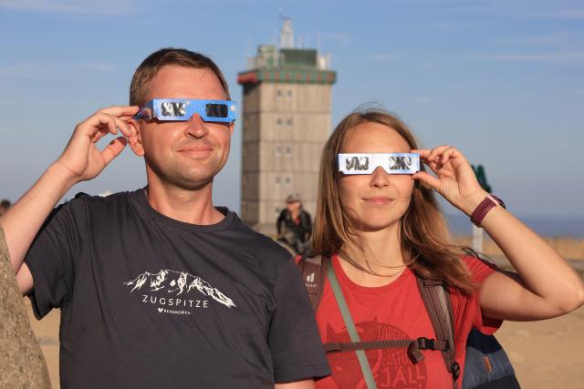 12 August 2026, Saxony-Anhalt, Schierke: Christian Schuder and Kylie Wersinger from Lower Saxony observe the partial solar eclipse in the Harz Mountains on the Brocken. Photo: Matthias Bein/dpa