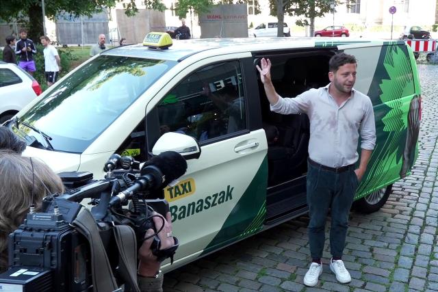 SCREENSHOT - 12 August 2026, Berlin: Felix Banaszak, chairman of Alliance 90/The Greens, stands in front of his taxi. As part of the campaign leading up to the state elections, Green Party leader Banaszak is driving potential voters around the area. Photo: Manuel Genolet/dpa