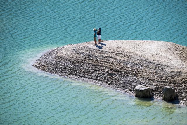 13 August 2026, Bavaria, Vorderriss: Two people out for a walk are standing on the exposed bed of the Sylvenstein Reservoir, which lies on the border with Tyrol. Photo: Peter Kneffel/dpa