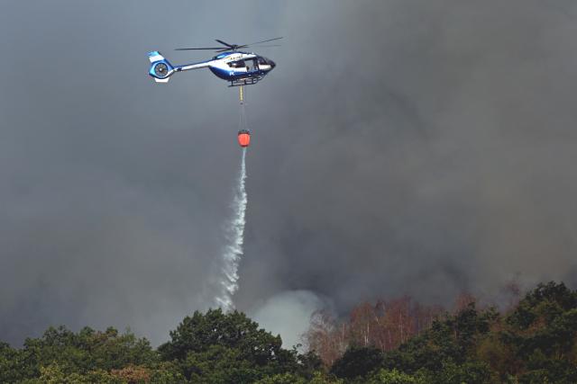 14 August 2026, North Rhine-Westphalia, Hürtgenwald: A police helicopter equipped with an external water tank is assisting with firefighting efforts at the forest fire in the Hürtgenwald. Several hundred hectares of forest are ablaze. Photo: Federico Gambarini/dpa