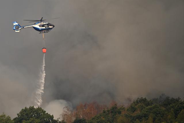 14 August 2026, North Rhine-Westphalia, Hürtgenwald: A police helicopter equipped with an external water tank is assisting with firefighting efforts at the forest fire in the Hürtgenwald. Several hundred hectares of forest are ablaze. Photo: Federico Gambarini/dpa