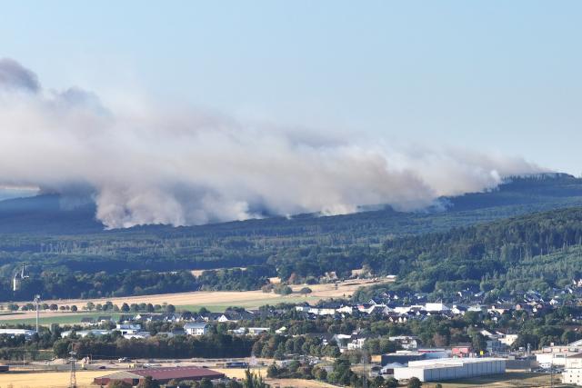 14 August 2026, North Rhine-Westphalia, Düren: Thick smoke from a forest fire rises above the Hürtgenwald (drone footage). Due to the forest fire in the municipality of Hürtgenwald, the district of Gey-home to some 1,800 people-was evacuated. Photo: Sascha Thelen/dpa