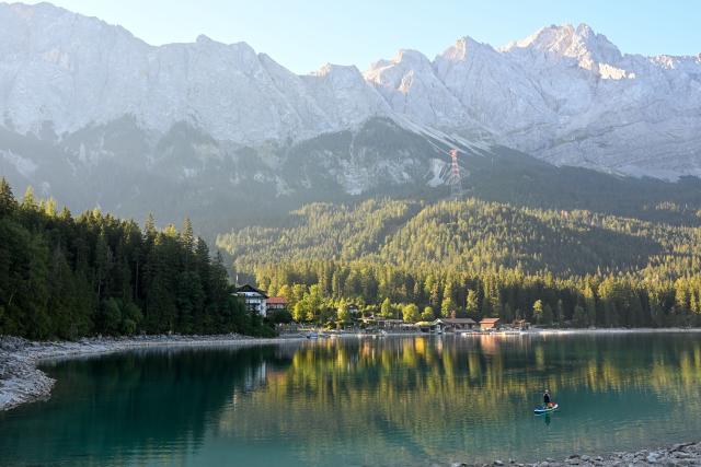 14 August 2026, Bavaria, Grainau: A view of Lake Eibsee near Grainau in the early morning hours, before the rush of day-trippers and vacationers arrives at the mountain lake that has become famous worldwide through social media. The rise in mass tourism regularly leads to a veritable flood of visitors. Residents living around the Eibsee are increasingly suffering from the heavy traffic, streets clogged with parked cars, and the large crowds. Photo: Marius Bulling/onw-images/dpa