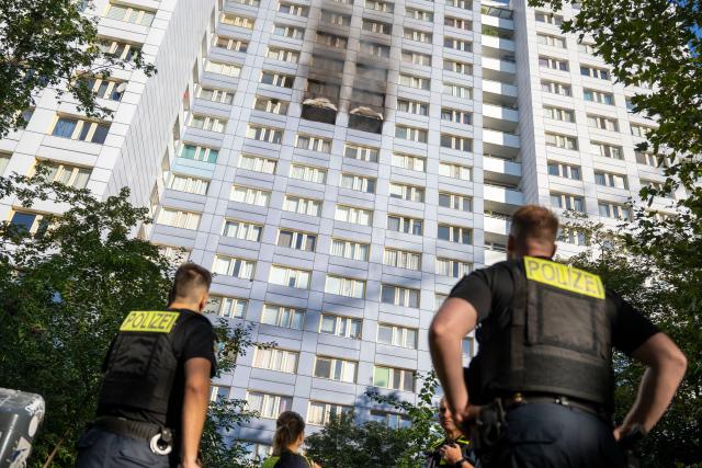 14 August 2026, Berlin: Police officers are standing in front of a high-rise building during a fire in Friedrichshain. Photo: Christophe Gateau/dpa