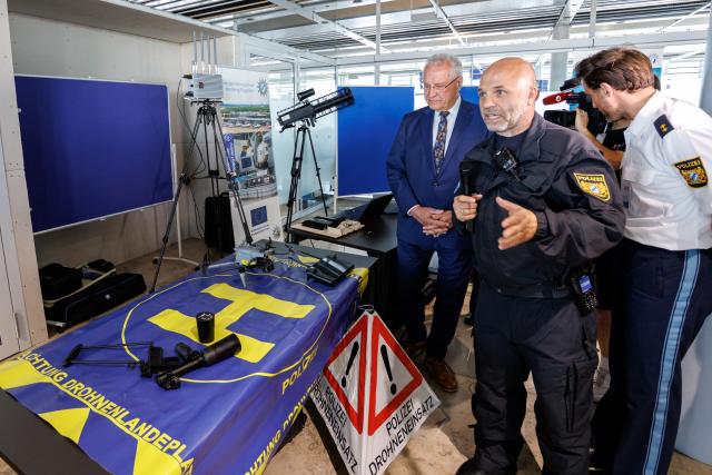 14 August 2026, Bavaria, Nuremberg: Christian Steidl (M), head of the drone operations unit at the Drone Competence and Defense Center (DKAZ), presents various drone detection and defense tools alongside Joachim Herrmann (L, CSU), Bavaria's Minister of the Interior, at a press conference at Nuremberg Airport, where they showcased various tools for drone detection and defense. To best prepare the Bavarian police for current and future developments in this area and to further expand existing capabilities, the Drone Competence and Defense Center (DKAZ) began operations in Erding on April 1, 2026. Photo: Daniel Karmann/dpa