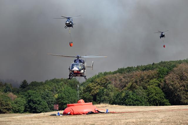 14 August 2026, North Rhine-Westphalia, Hürtgenwald-Großhau: Helicopters are flying in to collect water in external water tanks for use in fighting the forest fire in the Huertgenwald. Several hundred hectares of forest are ablaze. Photo: Federico Gambarini/dpa