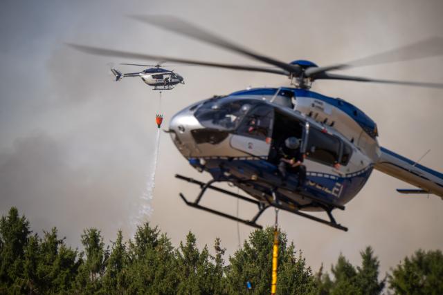 14 August 2026, North Rhine-Westphalia, Huertgenwald-Grosshau: A police helicopter drops water from an external water tank onto a forest fire in the Hürtgenwald. Several hundred hectares of forest are ablaze. Photo: Harald Tittel/dpa