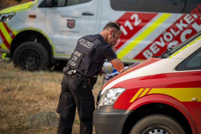 14 August 2026, North Rhine-Westphalia, Huertgenwald-Großhau: A police officer reviews documents while responding to a forest fire in the Hürtgen Forest. Photo: Harald Tittel/dpa