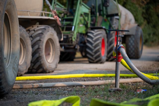 14 August 2026, North Rhine-Westphalia, Huertgenwald-Großhau: A hose is connected to a fire hydrant to fill a water tank behind a farm tractor as firefighters battle a forest fire in the Hürtgen Forest. Photo: Harald Tittel/dpa