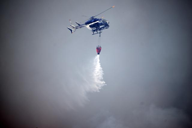 14 August 2026, North Rhine-Westphalia, Huertgenwald-Großhau: A police helicopter drops water from an external tank onto a forest fire in the Hürtgenwald. Several hundred hectares of forest are ablaze. Photo: Federico Gambarini/dpa