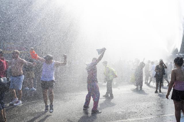 15 August 2026, Berlin: Participants in the "Rave The Planet Parade 2026" demonstration cool off under the mist from a police water cannon. Photo: Christophe Gateau/dpa