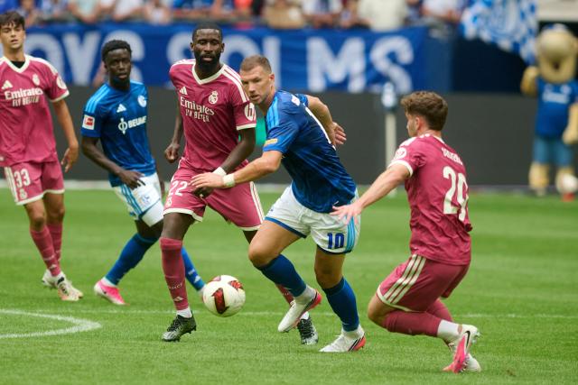 16 August 2026, North Rhine-Westphalia, Gelsenkirchen: Schalke 04's Edin Dzeko in action with Real Madrid's Antonio Ruediger (L) during a friendly soccer match between FC Schalke 04 and Real Madrid CF at VELTINS-Arena, held to celebrate the stadium's 25th anniversary. Photo: Bernd Thissen/dpa - IMPORTANT NOTICE: In accordance with the regulations of the Bundesliga and the German Football Association (DFB), it is prohibited to use or allow the use of photographs taken in the stadium and/or during the game in the form of sequential images and/or video-like photo series.