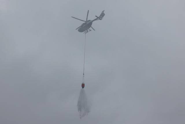 15 August 2026, Baden-Württemberg, Schramberg: A police helicopter drops water on a wildfire on a steep slope near Schramberg in the Rottweil district. Firefighters are attacking the flames on the slope from three sides. This has so far prevented the fire from spreading, particularly toward an adjacent residential area. Photo: Philipp von Ditfurth/dpa