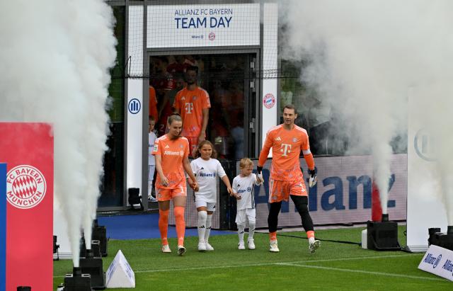 17 August 2026, Bavaria, Munich: Bayern Munich's Ena Mahmutovic (L) and goalkeeper Manuel Neuer walk onto the field past fog machines, during the German Bundesliga club's training and fan day. Photo: Peter Kneffel/dpa - IMPORTANT NOTICE: In accordance with the regulations of the Bundesliga and the DFB (German Football Association), it is prohibited to use or allow the use of photographs taken in the stadium and/or during the game in the form of sequential images and/or video-like photo series.