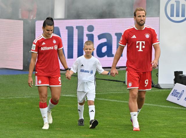 17 August 2026, Bavaria, Munich: Bayern Munich's Jovana Damnjanovic (L) and Harry Kane  walk onto the field during the German Bundesliga club's training and fan day. Photo: Peter Kneffel/dpa - IMPORTANT NOTICE: In accordance with the regulations of the Bundesliga and the DFB (German Football Association), it is prohibited to use or allow the use of photographs taken in the stadium and/or during the game in the form of sequential images and/or video-like photo series.