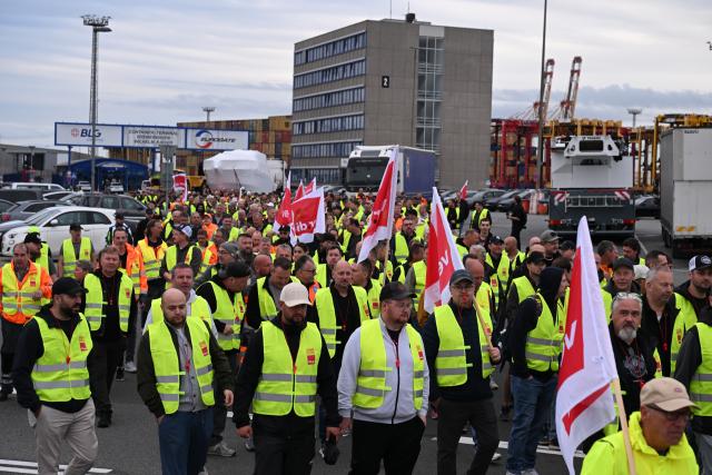18 August 2026, Bremen, Bremerhaven: Workers stand together during a Verdi rally held in conjunction with the warning strike at the Port of Bremerhaven. The union is currently negotiating with the employers' association ZDS over the wages of port workers. The employers' latest offer was rejected by the workers. Photo: Sina Schuldt/dpa