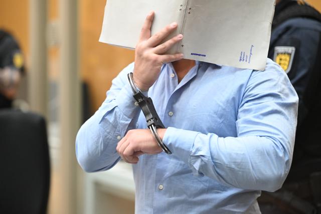 18 August 2026, Baden-Württemberg, Stuttgart (Stammheim): A defendant in a national security trial against three Ukrainians accused of acting as agents on behalf of a Russian intelligence service stands in the courtroom of the Stuttgart Higher Regional Court in Stammheim. The Ukrainian defendants are alleged to have sent two packages containing GPS trackers to Ukraine via a Ukrainian postal service provider in March 2025 in order to investigate the shipping routes and transport procedures of the package delivery service. Photo: Marijan Murat/dpa