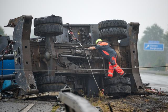 18 August 2026, North Rhine-Westphalia, Kamen: Employees of a recovery company are preparing to use steel cables to right an overturned construction crane that is lying across the median of the A2 highway after it slid off a heavy-duty truck in an accident. As a result, the highway is blocked in the direction of Hannover and Oberhausen. Photo: Bernd Thissen/dpa