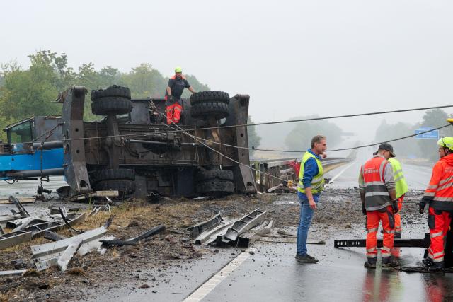 18 August 2026, North Rhine-Westphalia, Kamen: Employees of a salvage company are preparing to use steel cables to right an overturned construction crane that is lying across the median of the A2 highway after it slipped off a heavy-duty transport truck in an accident. As a result, the highway is blocked in the direction of Hannover and Oberhausen. Photo: Bernd Thissen/dpa