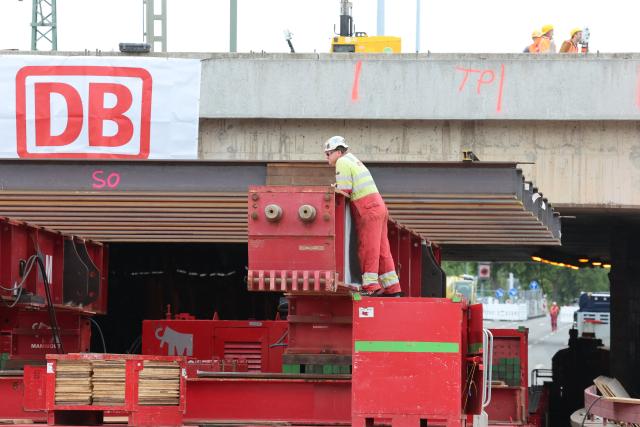 18 August 2026, Thuringia, Erfurt: A self-propelled modular transporter is positioned beneath the bridge during the demolition of a 38-meter-long, 1,800-metric-ton section of the bridge. Inspections revealed that a component of the railroad overpass, built in the 1970s, may be affected by stress corrosion cracking, so it is being completely replaced. Photo: Bodo Schackow/dpa