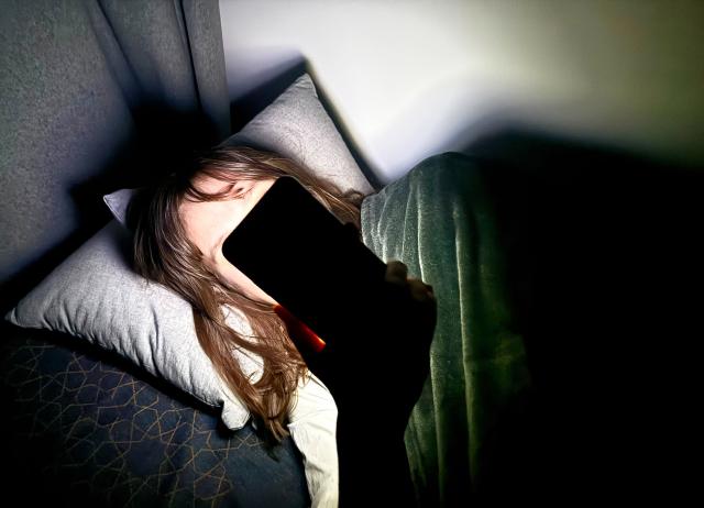 FILED - 21 January 2026, Berlin: File Photo - A woman lies on a bed and holds a smartphone in front of her face. Photo: Alicia Windzio/-/dpa