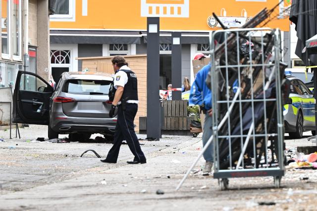 21 August 2026, Hesse, Hofgeismar: A police officer examines a damaged carnear the scene where a car sped through the pedestrian zone at high speed in Hofgeismar. Photo: Florian Wiegand/dpa