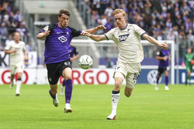 22 August 2026, Saxony, Aue: Erzgebirge Aue's Tim Maciejewski (L) and Hoffenheim's Mats Rots battle for the ball during the German Cup (DFB Pokal) first round soccer match between Erzgebirge Aue vs TSG 1899 Hoffenheim at Erzgebirgsstadion. Photo: Jan Woitas/dpa - IMPORTANT NOTICE: Bundesliga and DFB regulations prohibit any use of photographs as image sequences and/or quasi-video.