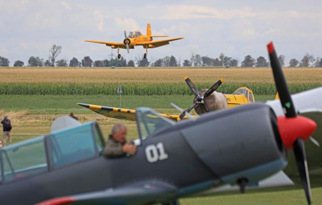 22 August 2026, Saxony-Anhalt, Ballenstedt: Airplanes are parked at the Ballenstedt/Harz airfield during the International Radial-Engine Airshow, while a Zlin Z 37 comes in on approach. Numerous pilots brought historic aircraft, from the Yak-11 to the Lockheed L-12, to the Harz region, though poor weather limited the number of in-flight demonstrations. Photo: Matthias Bein/dpa