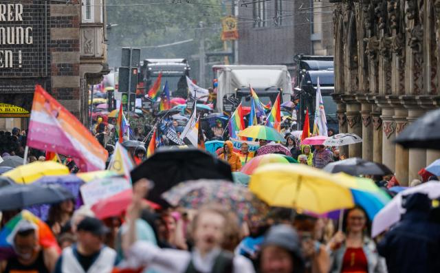 22 August 2026, Bremen: Participants in the Christopher Street Day (CSD) parade walk along Osterdeich behind a police vehicle displaying a banner with the Pride Parade's motto: "Generations Full of Pride-Happy, Visible, Strong." Photo: Focke Strangmann/dpa