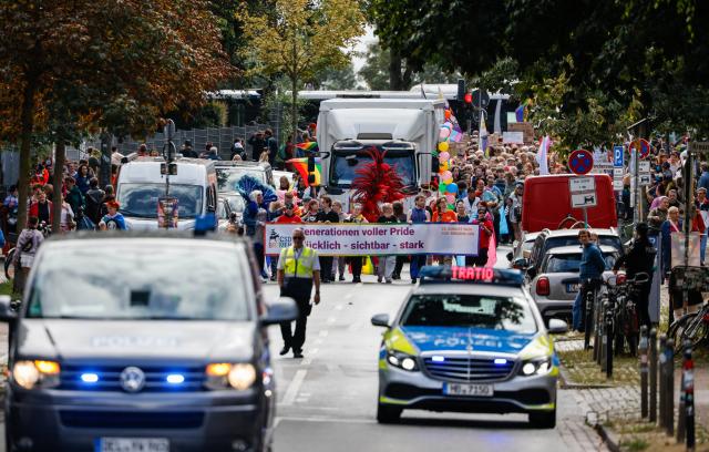 22 August 2026, Bremen: Participants in the Christopher Street Day (CSD) parade walk along Osterdeich behind a police vehicle displaying a banner with the Pride Parade's motto: "Generations Full of Pride-Happy, Visible, Strong." Photo: Focke Strangmann/dpa