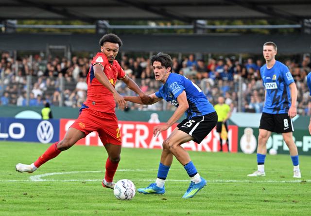 22 August 2026, Trier: Leipzig's Tidiam Gomis (L) and Eintracht Trier's Gianluca Pelzer battle for the ball during the German Cup (DFB Pokal) first round soccer match between Eintracht Trier and RB Leipzig at Moselstadion Photo: Harald Tittel/dpa - IMPORTANT NOTICE: Bundesliga and DFB regulations prohibit any use of photographs as image sequences and/or quasi-video.