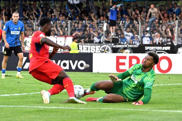 22 August 2026, Trier: Leipzig's Ridle Baku (L) in action against Eintracht Trier goalkeeper Leon-Oumar Wechsel during the German Cup (DFB Pokal) first round soccer match between Eintracht Trier and RB Leipzig at Moselstadion Photo: Harald Tittel/dpa - IMPORTANT NOTICE: Bundesliga and DFB regulations prohibit any use of photographs as image sequences and/or quasi-video.