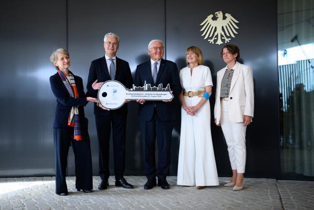 24 August 2026, Berlin: German President Frank-Walter Steinmeier and his wife Elke Buedenbender accept the symbolic key for their temporary official residence, the modular wooden "Amtssitz am Spreebogen." They were joined by Petra Wesseler (BBR), Alexander von Erdély (BImA), and Doerte Dinger (Office of the Federal President). Located across from the Federal Chancellery, the colorful building will house the president's staff for up to eight years while Bellevue Palace and its administrative offices undergo extensive renovations. Photo: Bernd von Jutrczenka/dpa