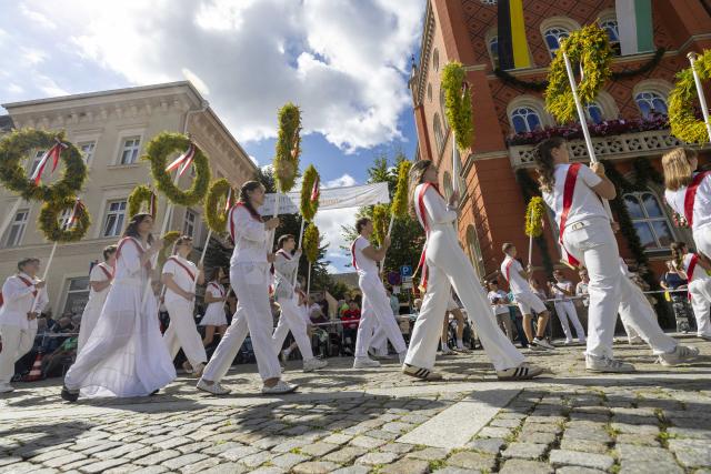 24 August 2026, Saxony, Kamenz: Students dressed in white carrying traditional flags on their shoulders or holding flower wreaths in their hands take part in the forestry festival parade. Photo: Daniel Wagner/dpa