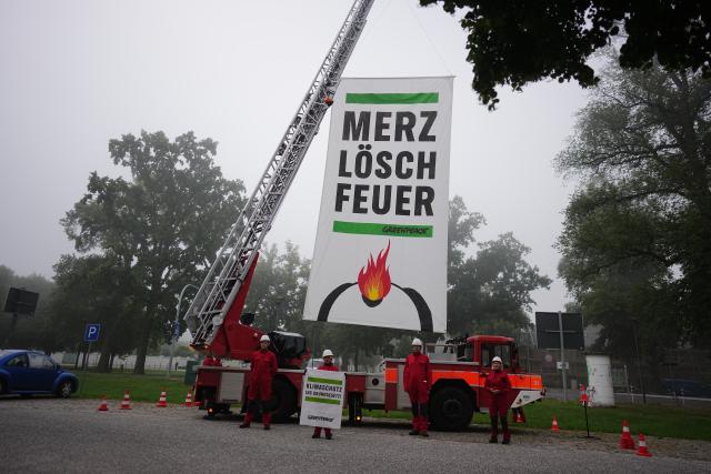 25 August 2026, Brandenburg, Neuhardenberg: Greenpeace activists hung a sign reading "Merz, Put Out the Fire" on a fire truck during a climate change protest held on the sidelines of the German government's closed-door meeting. The German government is gathering in Neuhardenberg for a two-day closed-door meeting. Photo: Kay Nietfeld/dpa