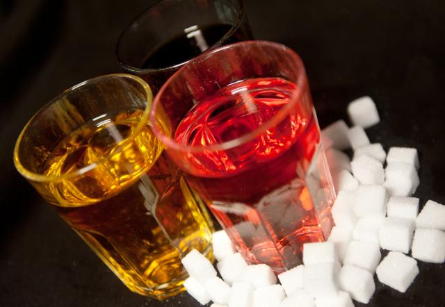 FILED - 23 August 2016, Berlin: Three glasses filled with red lemonade, coke and energy drink placed on a desk next to sugar cubes. Photo: Monika Skolimowska/dpa
