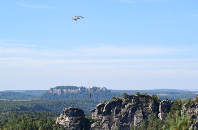 27 August 2026, Saxony, Hohnstein: A helicopter is clearing storm damage in Saxon Switzerland near Lake Amsel and in the area of the Rathen Rock Stage; Königstein Fortress can be seen in the background. Photo: Robert Michael/dpa