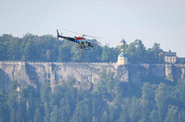 27 August 2026, Saxony, Hohnstein: A helicopter is on the scene helping to clear storm damage in Saxon Switzerland at Amselsee and near the Rathen Rock Theater; Koenigstein Fortress can be seen in the background. Photo: Robert Michael/dpa