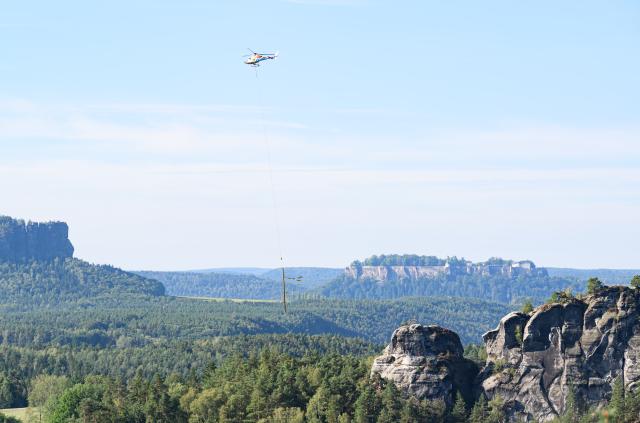 27 August 2026, Saxony, Hohnstein: A helicopter is on the scene helping to clear storm damage in Saxon Switzerland at Lake Amsel and near the Rathen Open-Air Theater; Koenigstein Fortress can be seen in the background. Photo: Robert Michael/dpa