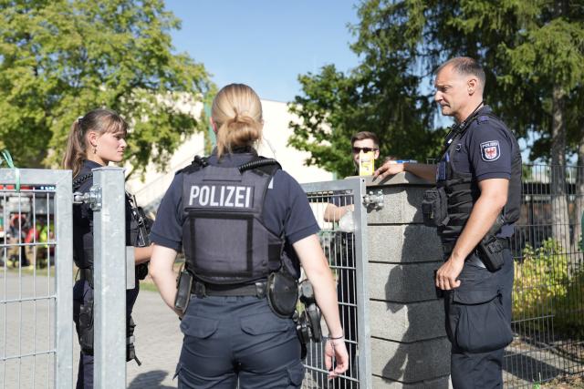 27 August 2026, Brandenburg, Gosen-Neu-Zittau: Police officers stand in front of a school in Gosen-Neu Zittau, where a woman and a man were killed in a violent incident. Photo: Manuel Genolet/dpa