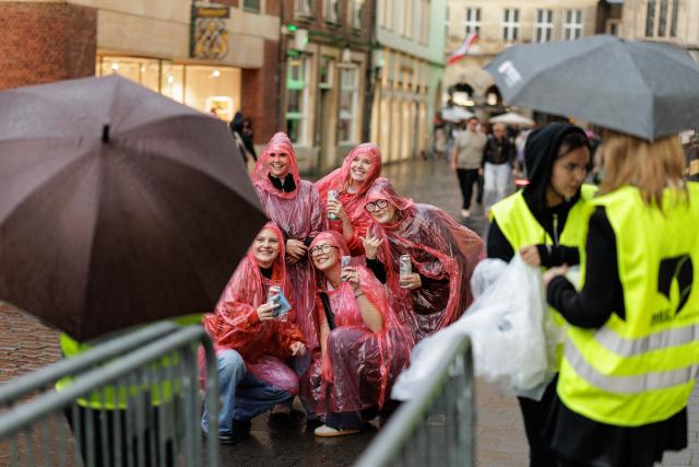 28 August 2026, North Rhine-Westphalia, Muenster: Young volunteers in rain ponchos pose for a group photo during the celebrations for the state's 80th anniversary in Muenster. Photo: David Ebener/dpa