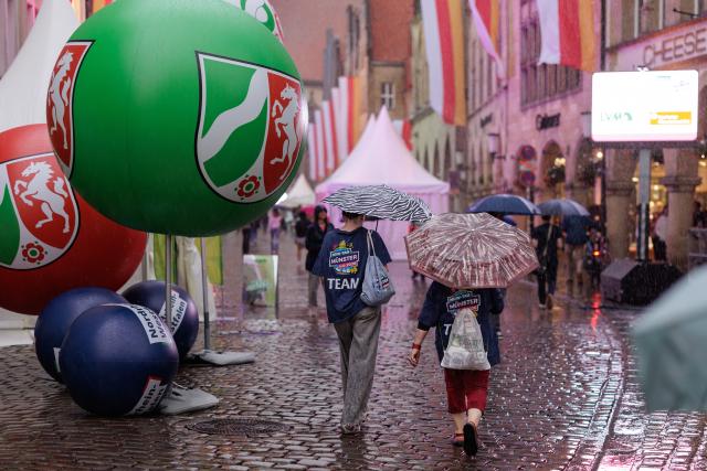28 August 2026, North Rhine-Westphalia, Muenster: A balloon bearing the North Rhine-Westphalia state coat of arms floats over the Prinzipalmarkt in Muenster during a rain shower as part of the celebrations marking the state's 80th anniversary. Photo: David Ebener/dpa