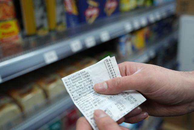 FILED - 05 January 2026, Hamburg: FILE PHOTO - A man holds up his receipt in front of a shelf of goods in a small grocery store. Photo: Marcus Brandt/dpa