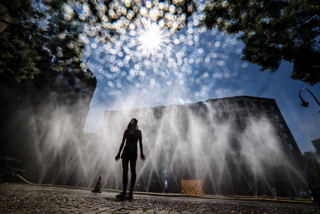 FILED - 29 July 2026, North Rhine-Westphalia, Cologne: FILE PHOTO - A woman stands in front of a hose spraying a mist of water during a heatwave in Cologne. Photo: Oliver Berg/dpa