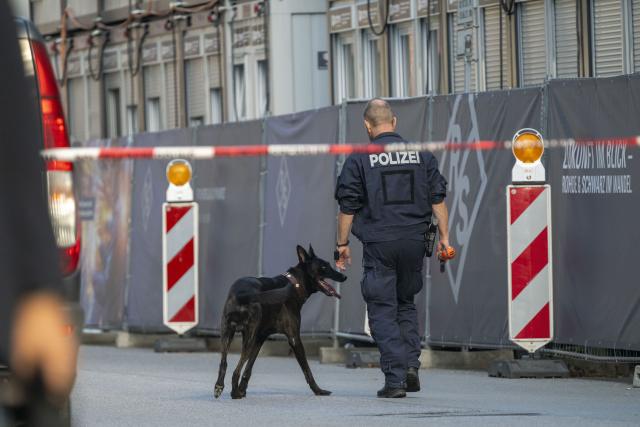 03 September 2026, Bavaria, Munich: A police officer with a police detection dog walks past a company property. Following an arson attack on a construction site in Munich, the Bavarian State Criminal Police Office (LKA) suspects an attempted attack against a defense contractor. Several incendiary devices were thrown at the construction site early Thursday morning; two people were later arrested. Photo: Peter Kneffel/dpa