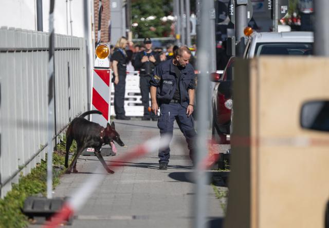 03 September 2026, Bavaria, Munich: A police officer with a police detection dog walks past a company property. Following an arson attack on a construction site in Munich, the Bavarian State Criminal Police Office (LKA) suspects an attempted attack against a defense contractor. Several incendiary devices were thrown at the construction site early Thursday morning; two people were later arrested. Photo: Peter Kneffel/dpa