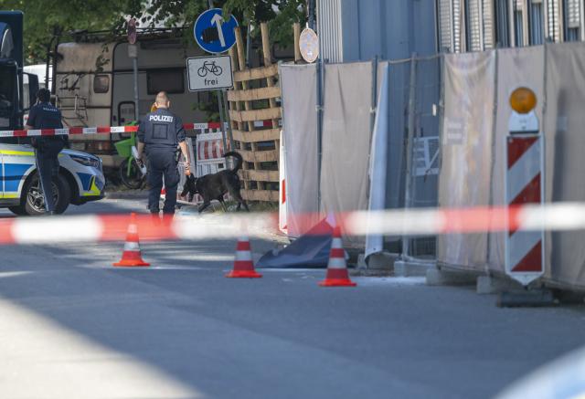 03 September 2026, Bavaria, Munich: A police officer with a police detection dog walks past a company property. Following an arson attack on a construction site in Munich, the Bavarian State Criminal Police Office (LKA) suspects an attempted attack against a defense contractor. Several incendiary devices were thrown at the construction site early Thursday morning; two people were later arrested. Photo: Peter Kneffel/dpa
