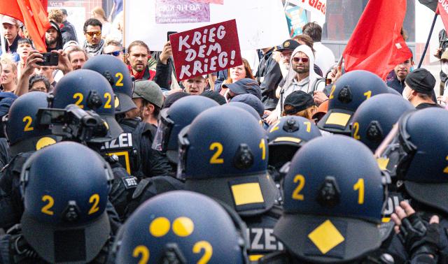 05 September 2026, North Rhine-Westphalia, Cologne: A participant holds a sign that reads "War on War" in front of police officers during a demonstration by the "Disarm Rheinmetall" protest camp in Cologne. Photo: Benjamin Westhoff/dpa