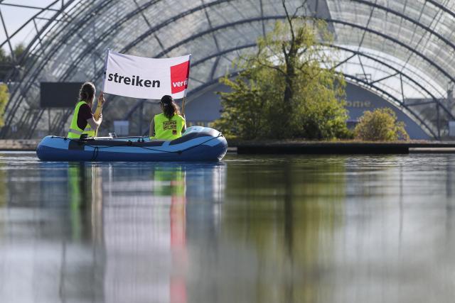 08 September 2026, Saxony, Leipzig: Employees of Leipziger Messe GmbH and its subsidiaries travel in a rubber boat carrying a banner that reads "We're on strike" across the lake in front of the Glass Hall at the exhibition grounds, as part of a warning strike. The union is demanding a pay raise that at least offsets inflation. Two rounds of collective bargaining have taken place so far. The third round of negotiations is scheduled for September 10. Photo: Jan Woitas/dpa
